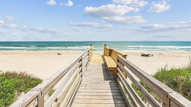 Una passerella di legno che conduce a una spiaggia sabbiosa con l'oceano sullo sfondo.