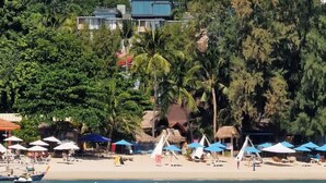 A beach with thatched-roof huts, palm trees, and a clear blue sea. - Villa Obsidian (Koh Samui)