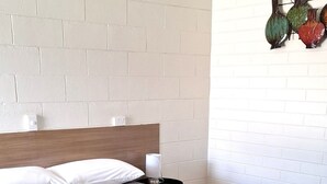A neatly made bed with a grey textured bedspread, two folded towels, and a bedside lamp.