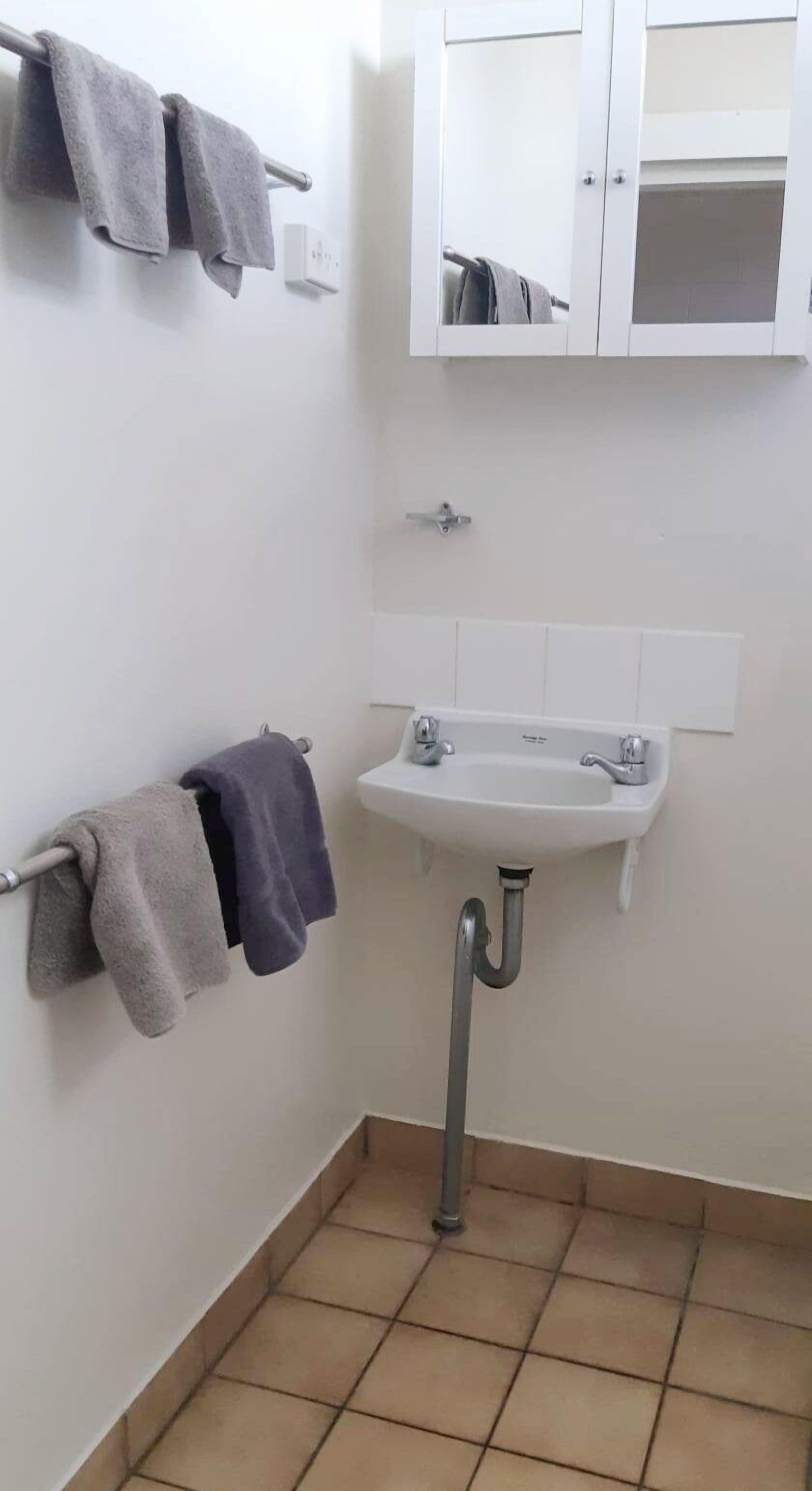 Een kleine badkamer met een witte wastafel, een spiegel en een handdoekhouder met twee handdoeken.