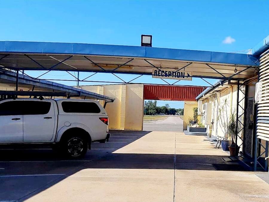 A reception area with a white SUV parked in front, a covered walkway, and a building with a sign that reads "RECEPTION".