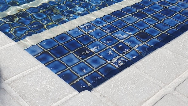 A swimming pool with blue mosaic tiles and a tiled deck.