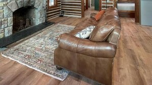 Un salón espacioso con chimenea de piedra, vigas de madera, un sofá de cuero y una alfombra grande.