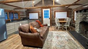 Interior acogedor de una cabaña con sofá de cuero, mesa de comedor, sillas y chimenea de piedra.