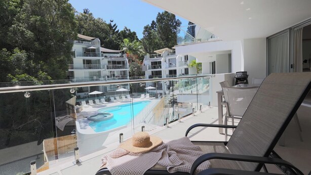 A balcony with a pool, lounge chairs, and a view of other buildings.