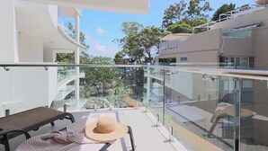 A modern balcony with glass railings overlooking a garden and neighboring buildings.