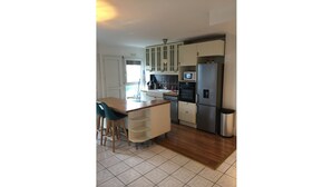 A modern kitchen with white cabinets, a stainless steel refrigerator, and a wooden dining table with chairs. - Appartement Accueillant à une Demi-heure de Paris (Viry-Châtillon)