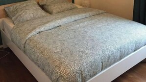 A bed with a patterned bedspread, a green textured wall, and a hanging light fixture. - Appartement Accueillant à une Demi-heure de Paris (Viry-Châtillon)
