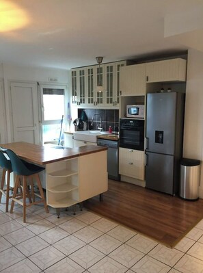 Una cocina moderna con armarios blancos, un refrigerador de acero inoxidable y una mesa de comedor de madera con sillas.