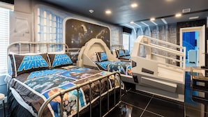 Een slaapkamer in Star Wars-thema met twee bedden, elk voorzien van passend Star Wars beddengoed en kussens. De kamer heeft een uniek ontwerp met een ruimte-thema wand en een trap naar een hoger niveau.