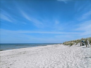 A sandy beach with a clear blue sky and calm sea.