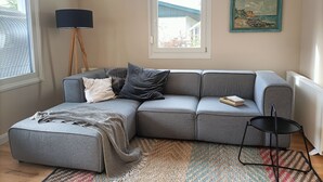 A living room with a grey sofa, a small ottoman, a black floor lamp, a patterned rug, and a painting on the wall. - Bungalow am Strand für die Ganze Familie (Insel Poel)