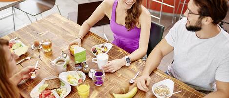 A group of people sitting around a wooden table with breakfast items like toast, fruit, and beverages.