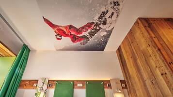 Una habitación de hotel con una cama, dos cabeceros verdes, una lámpara fijada a la pared y una obra de arte en el techo que representa a un snowboarder.