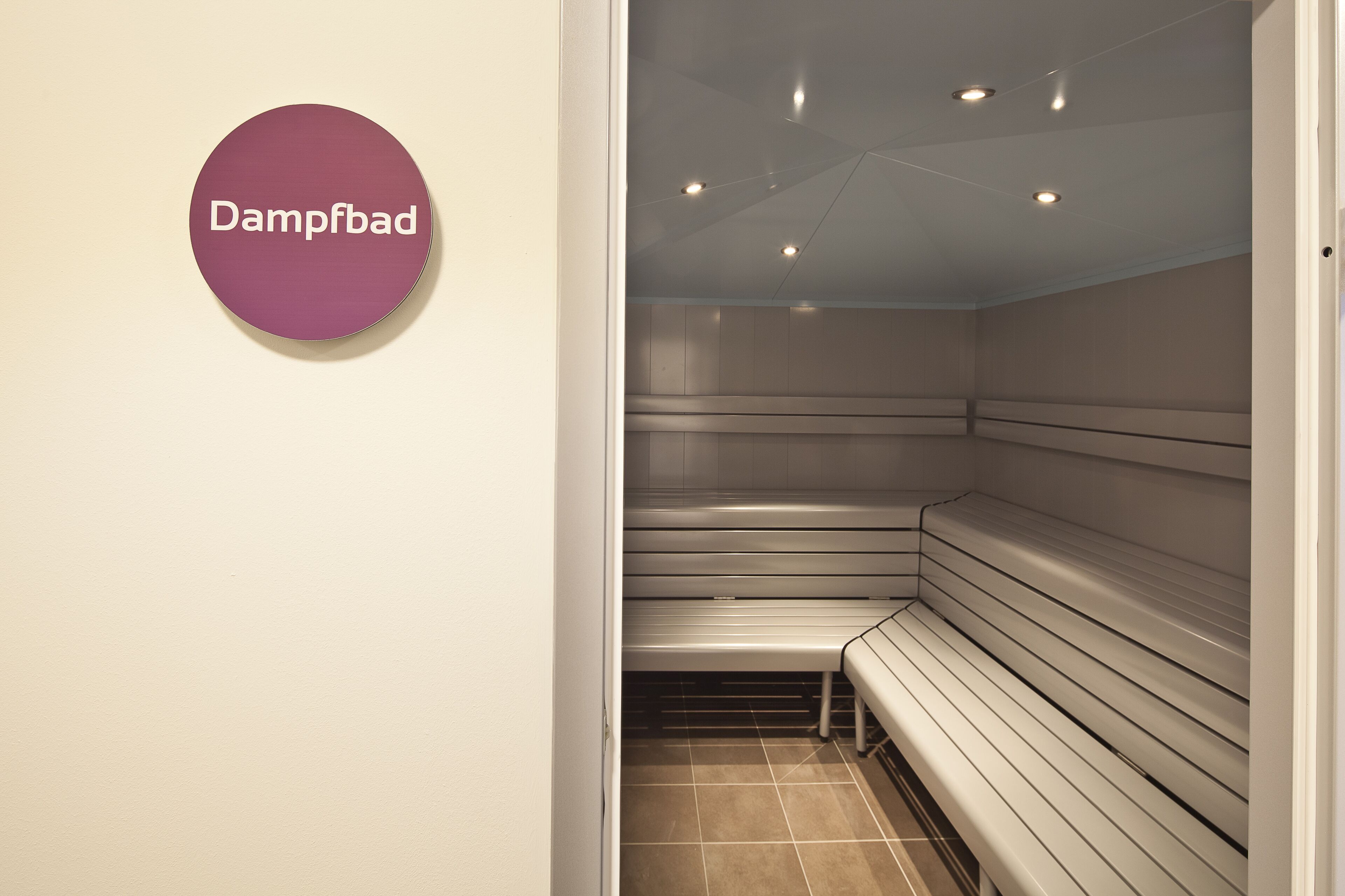 A sauna room with benches and a sign that reads 'Dampfbad.'