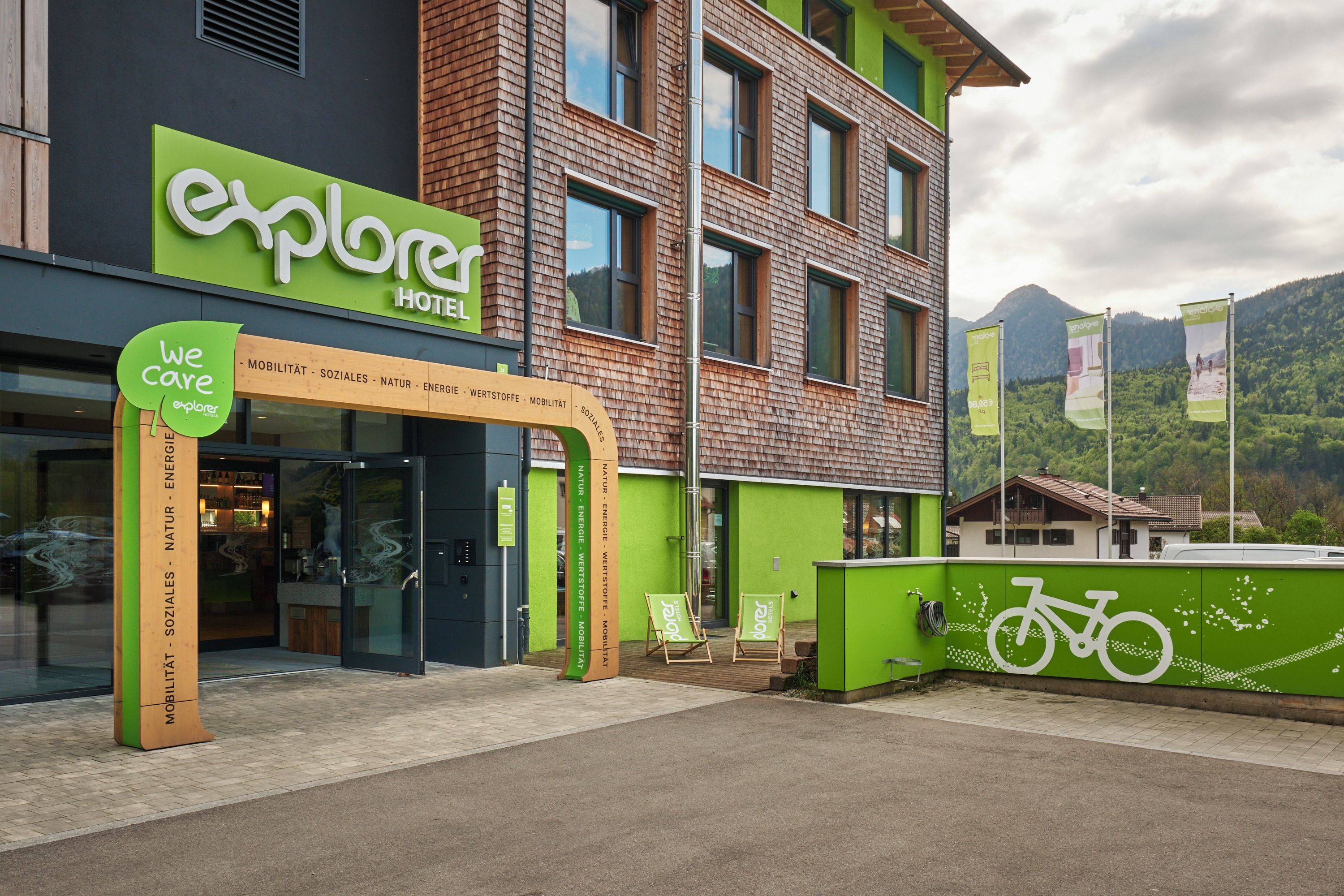 A hotel with a green facade, a sign reading 'explorer hotel,' and a signpost with 'we care' and various amenities listed.