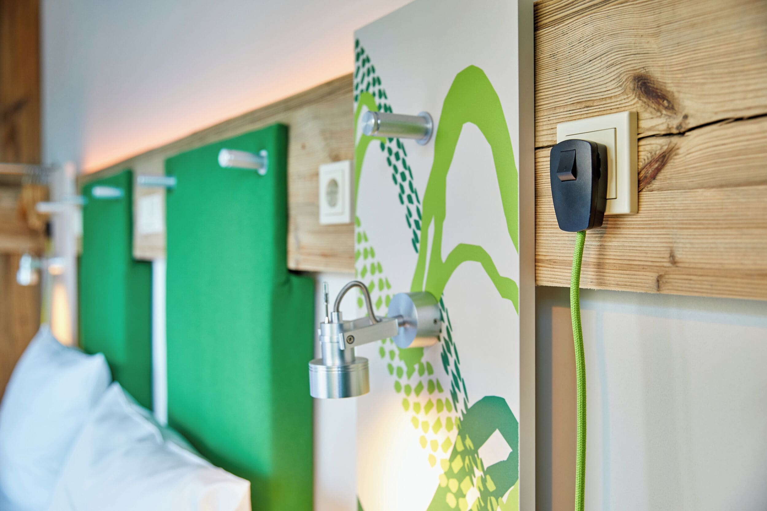 A hotel room with a green wall, a wooden panel, a power outlet, and a metal object on the wall.