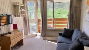 Une pièce chaleureuse avec un bureau en bois, un canapé bleu et une grande fenêtre donnant sur un paysage verdoyant.