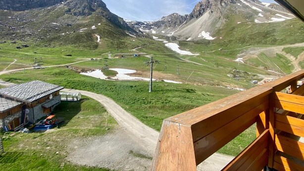 Un paysage de montagne avec un télésiège, un bâtiment doté d’un toit en pente et un banc en bois.