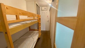 Un lit superposé dans un couloir, avec une porte et un appareil de climatisation en arrière-plan.