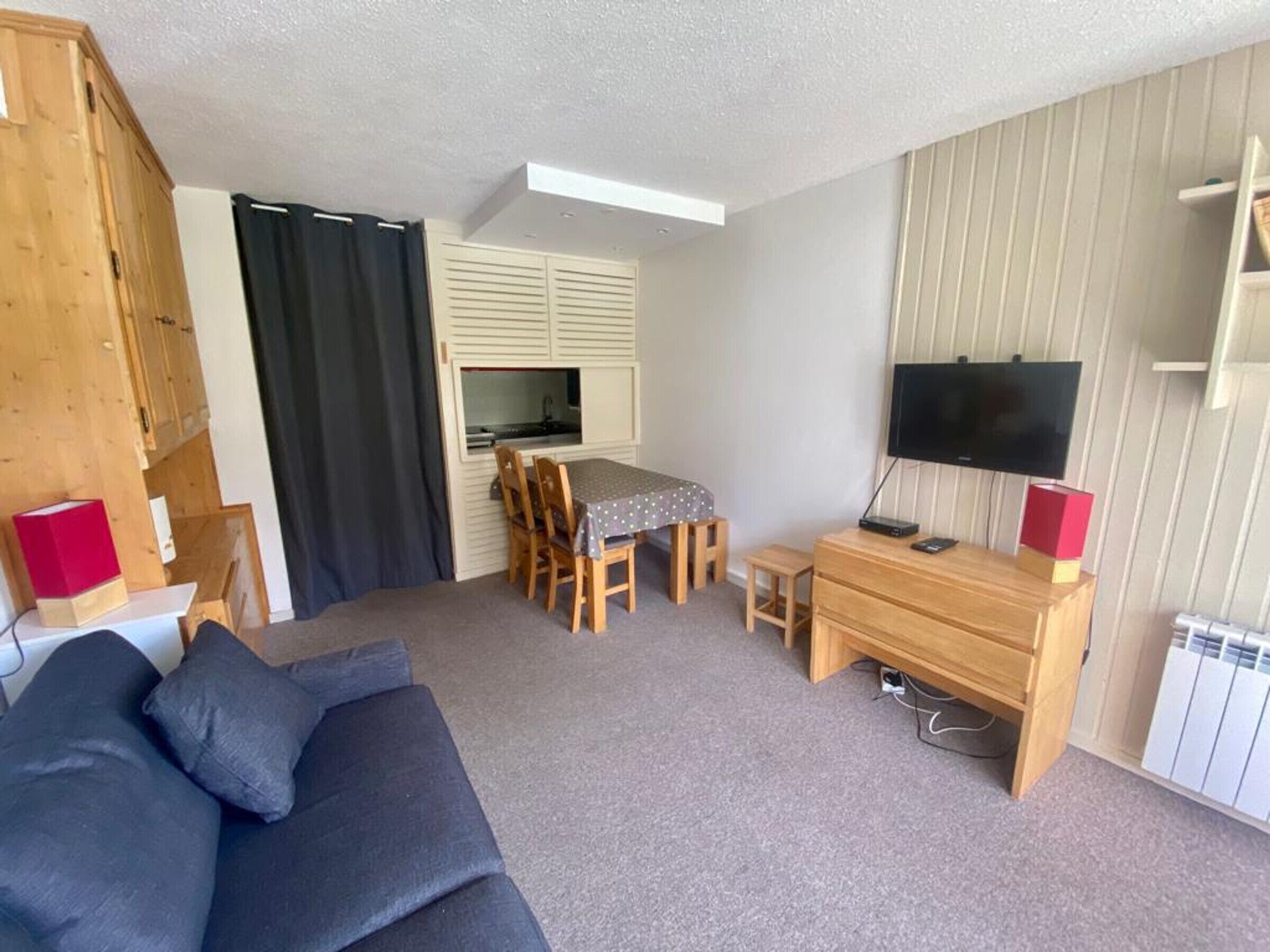 A compact living space with a sofa, a dining table with chairs, a TV, and a kitchenette.