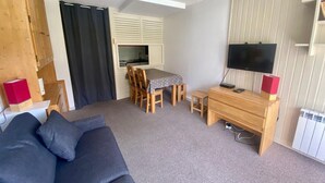 Un espace de vie compact comprenant un canapé, une table à manger avec des chaises, un téléviseur et un coin cuisine.