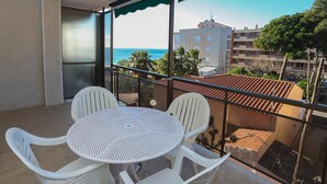 Un balcón con una mesa redonda y cuatro sillas, con vista a una zona costera con edificios y árboles.