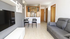 Una sala de estar moderna con un televisor de pantalla plana, un sofá gris y un comedor con dos sillas y una mesa.