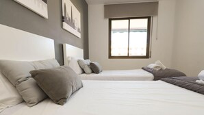 Habitación de hotel con dos camas, un ventanal grande y vistas a la ciudad.