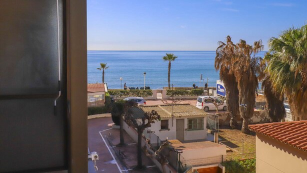 Vista desde un balcón sobre una zona costera con cielo despejado, palmeras y una furgoneta estacionada.