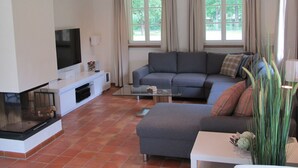 Een woonkamer met een hoekbank, een flatscreen televisie, een glazen salontafel en een open haard.