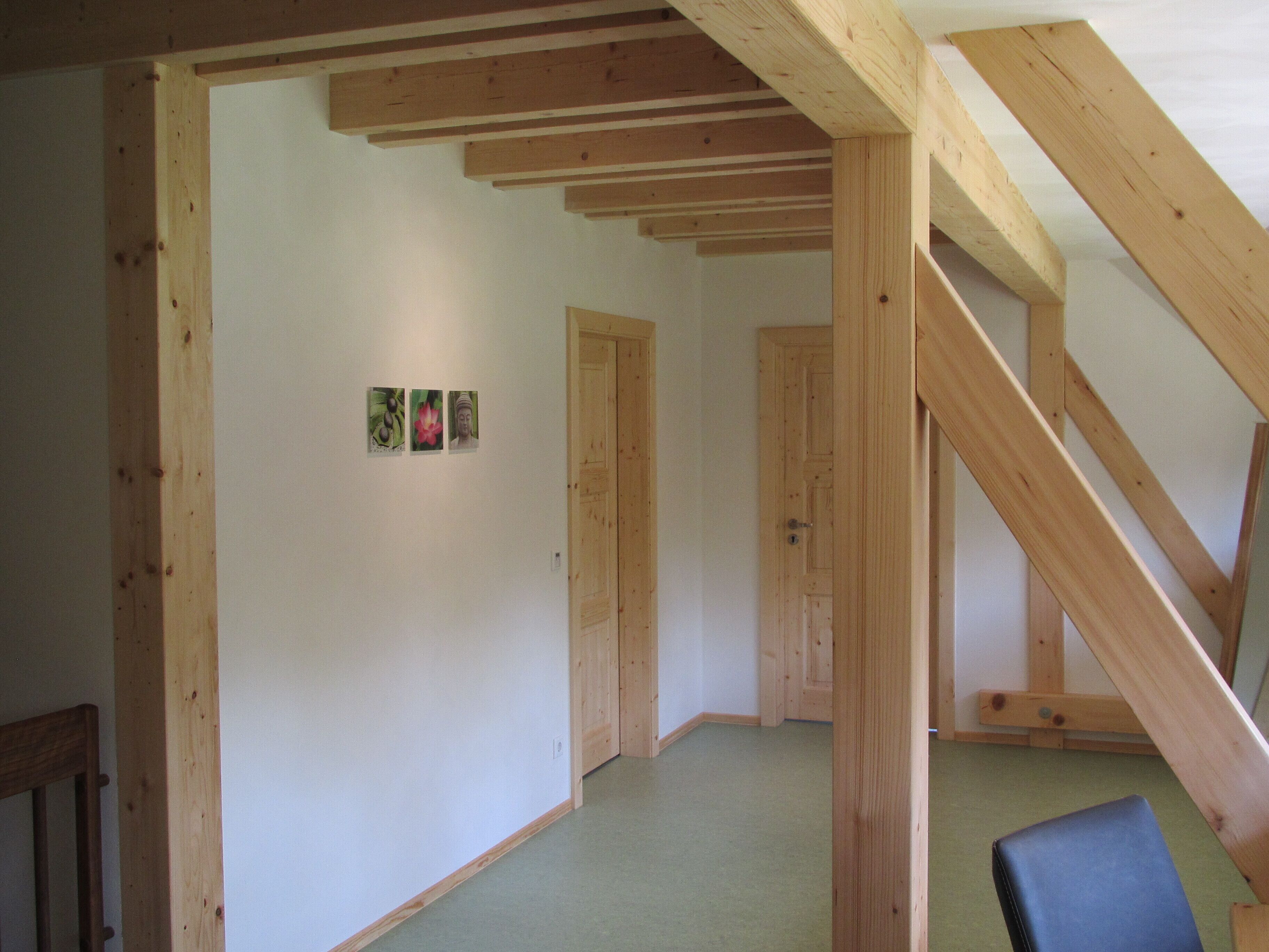 Una habitación con vigas de madera a la vista, alfombra verde y una puerta que da a otra habitación.