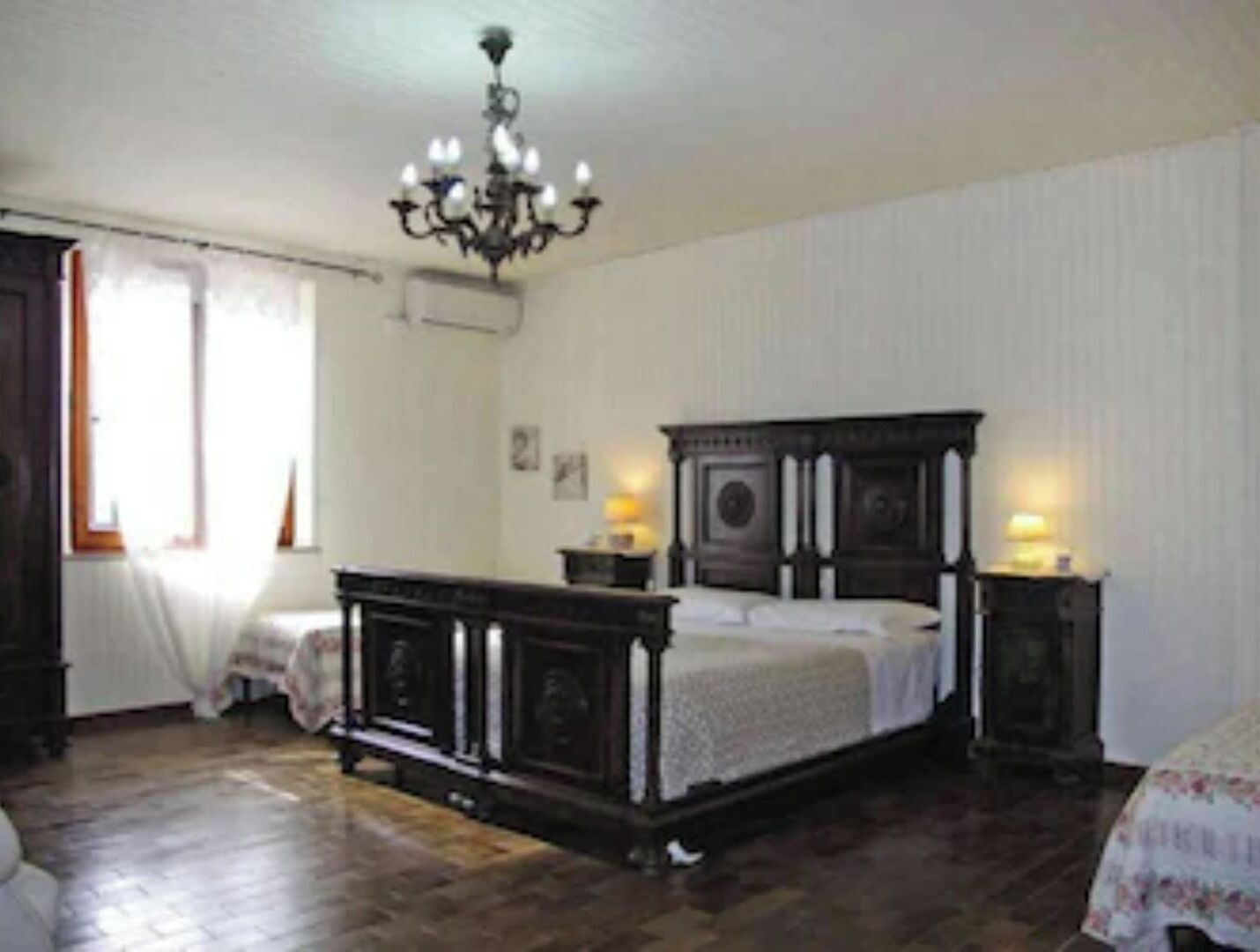 A bedroom with a large bed, a chandelier, and a wooden floor.