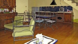 Un comedor con una mesa y sillas de madera, una cocina con azulejos azules y una escalera.