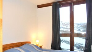 A bedroom with a bed, a nightstand with a lamp, and a window with curtains. - 3-room apartment at the foot of the slopes with balcony (Le Corbier)