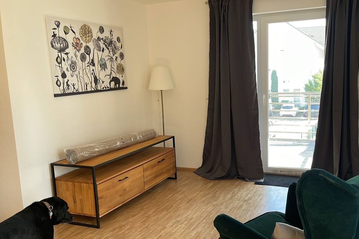A room with a wooden bench, a green chair, a lamp, and a large window with curtains.