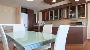 A modern kitchen with a glass dining table and white chairs, equipped with a microwave and cabinets. - Modern Apartment in Salou with Sea View (Salou)