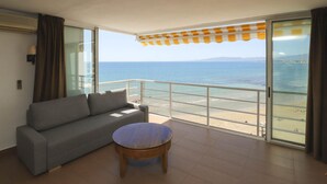 A balcony with a grey sofa and a round wooden table, overlooking a clear sea and distant mountains. - Modern Apartment in Salou with Sea View (Salou)