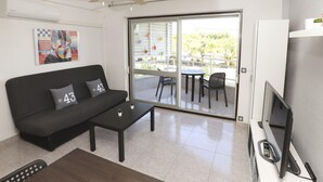 Ein modernes Wohnzimmer mit einer schwarzen Couch, einem Couchtisch, einem Deckenventilator, einem Fernseher und einer Glastür, die auf eine Außenpatio mit Stühlen und einem Tisch führt.