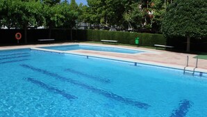 Ein rechteckiger Swimmingpool mit klarem, blauem Wasser, umgeben von einer Fliesenveranda und einem Heckenstreifen.