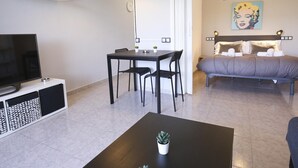Ein modernes Wohnzimmer mit Flachbildfernseher, einem Esstisch mit Stühlen, einem Couchtisch mit Pflanze und ein Schlafzimmer mit Bett und einem Bild an der Wand.
