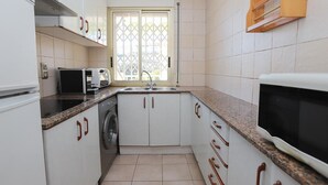 A compact kitchen with white cabinets, a built-in washing machine, a microwave, and a sink. - Cozy 2BR Apartment with Pool, Wi-Fi, and Private Terrace in Salou's Lively Tourist Area (Salou)