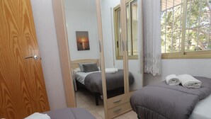A room with two beds, a wooden door, a mirror, and a window with a view of trees. - Cozy 2BR Apartment with Pool, Wi-Fi, and Private Terrace in Salou's Lively Tourist Area (Salou)