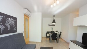 A modern living room with a grey sofa, a dining table with chairs, a black pendant light, and a flat-screen TV on a white cabinet. - Cozy 2BR Apartment with Pool, Wi-Fi, and Private Terrace in Salou's Lively Tourist Area (Salou)