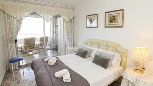 Ett hotellrum med en säng, en stol, ett bord med en lampa och två inramade tavlor på väggen.