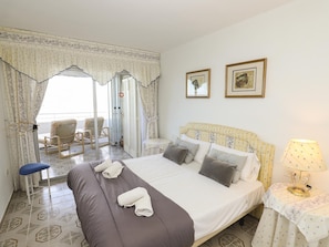 A hotel room with a bed, a chair, a table with a lamp, and two framed pictures on the wall.