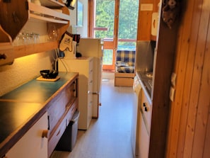 A compact kitchen with wooden cabinets, a small refrigerator, and a dining area with a plaid tablecloth.