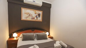 Habitación de hotel con cama, dos mesitas de noche con lámparas, un cuadro en la pared y una toalla doblada sobre la cama.