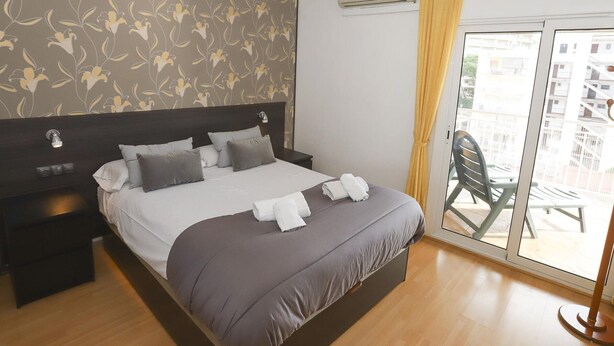 Habitación de hotel con cama, mesita de noche, aire acondicionado instalado en la pared y vista al balcón exterior.