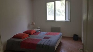 A bedroom with a bed, a nightstand, a lamp, a radiator, and a window. - Rez-de-villa (LE BEAUSSET)